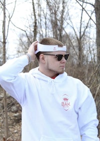 a man wearing a white hoodie and sunglasses is standing in the woods